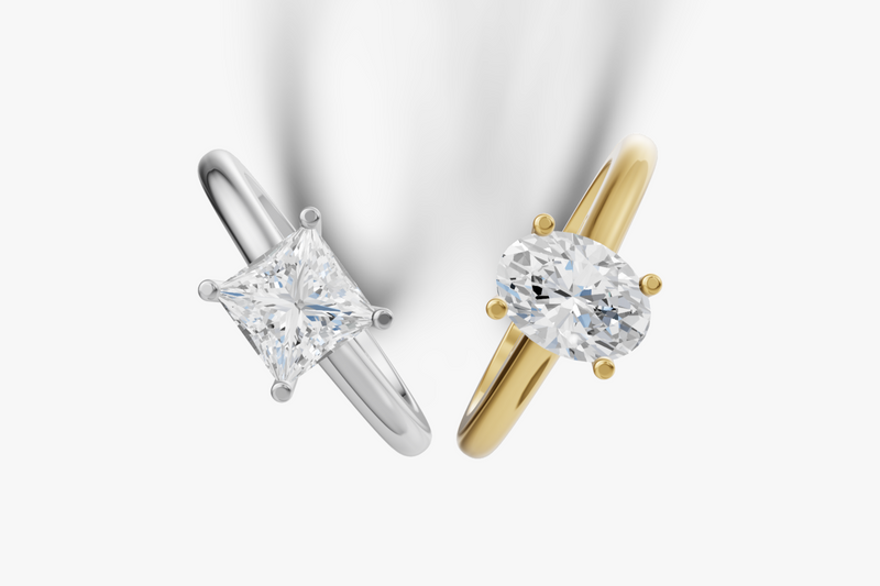 Pair of diamond engagement rings, one white gold and one gold, on a light gray background.